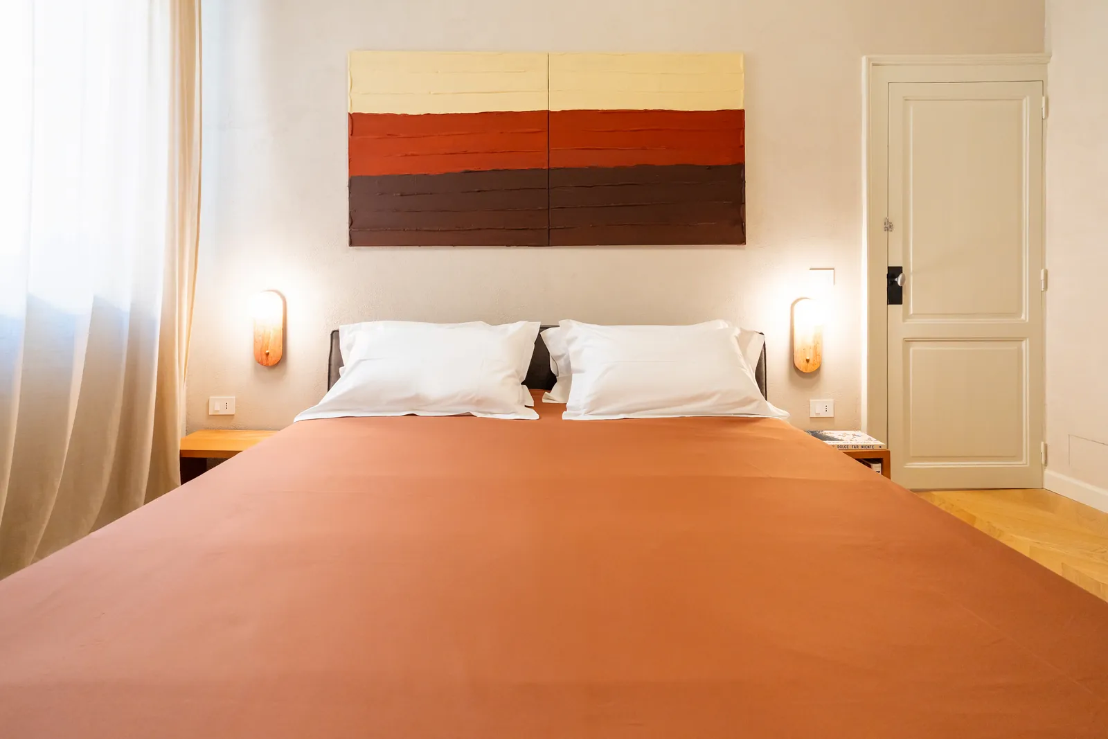 Letto matrimoniale visto di fronte, con cuscini bianchi e lampade da parete